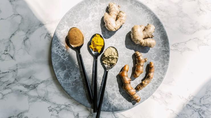 Spoons with spices and pieces of ginger and turmeric on platter