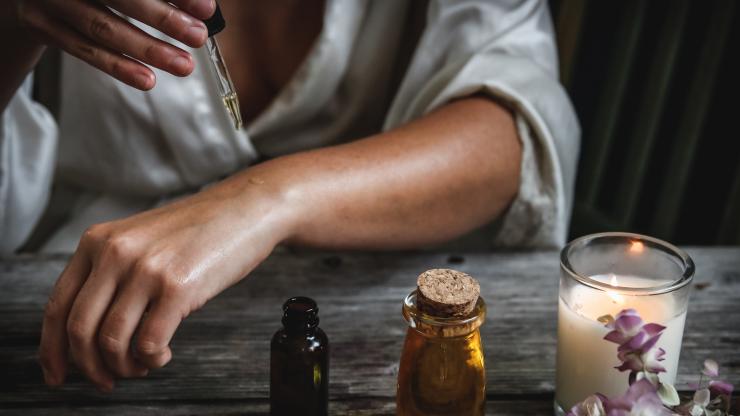 Woman puts body oil on her hand as a candle burns on the table next to her