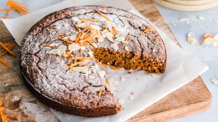 Carrot cake on a wooden cutting board dusted with powdered sugar and sprinkled with almond slivers