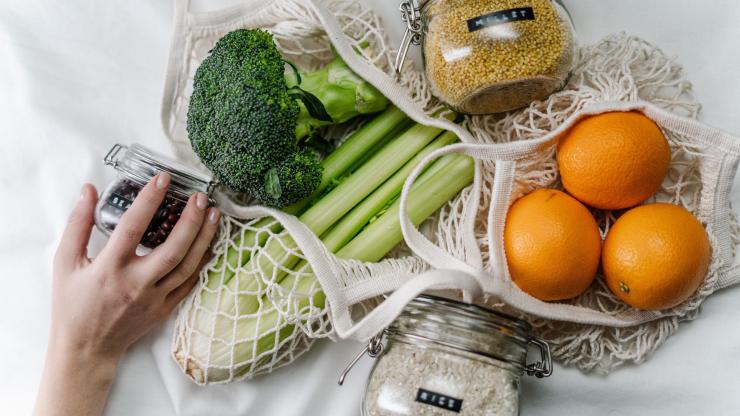 Broccoli, celery and oranges in reusable shopping bags, with grains in reusable glass jars