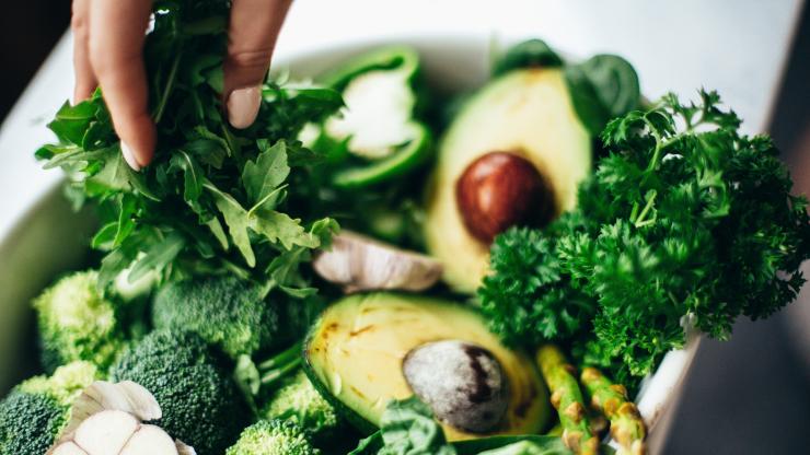 Bowl full of green veggies including avocado, asparagus, herbs, green pepper and broccoli