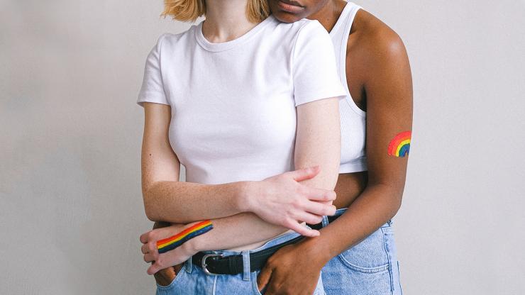 Two women with rainbows painted on their arms embrace.
