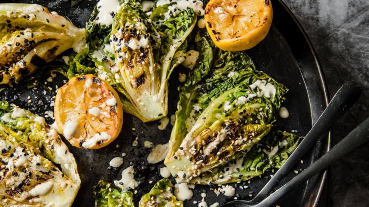 Chargrilled lettuce drizzled with lemon tahini, sesame seeds and lemons on a plate.