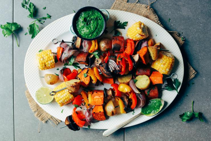 Veggie skewers of red peppers, onions, sweet potatoes and corn on a platter.