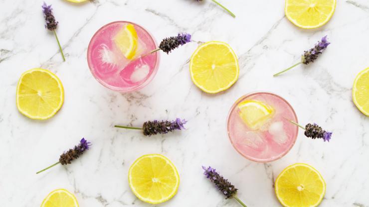 Overhead shot of lavender lemonade mocktails with lavender flowers and lemons on a table.