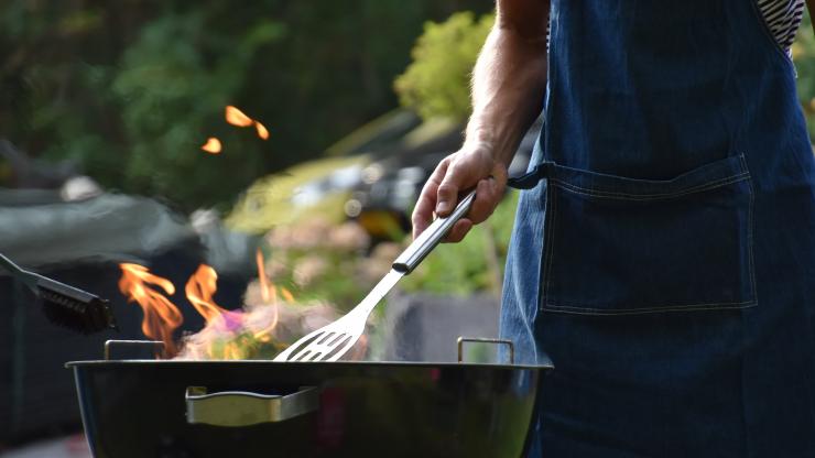 Man standing over a barbecue with a spatula.