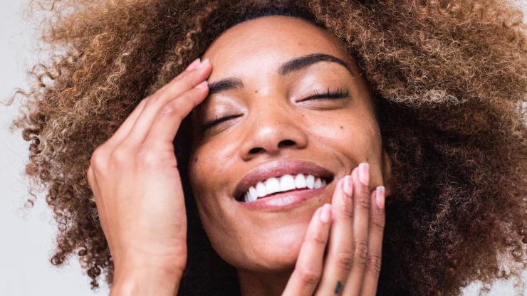 Woman smiles with eyes close and touches her face.