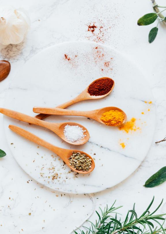 A marble table with sprigs of herbs wooden spoons holding colorful spices